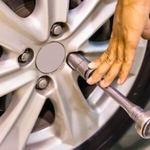 A close-up of a mechanic's hand using a wrench to tighten a lug nut on a silver car wheel.