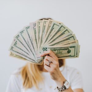 A person holding a fan of various US dollar bills (tens, twenties, fifties) that obscures their face, symbolizing wealth or saving.