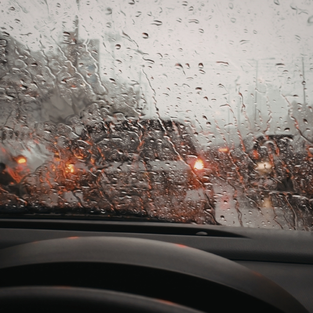 Raindrops on a car windshield with a wiper blade clearing the view during a spring shower.